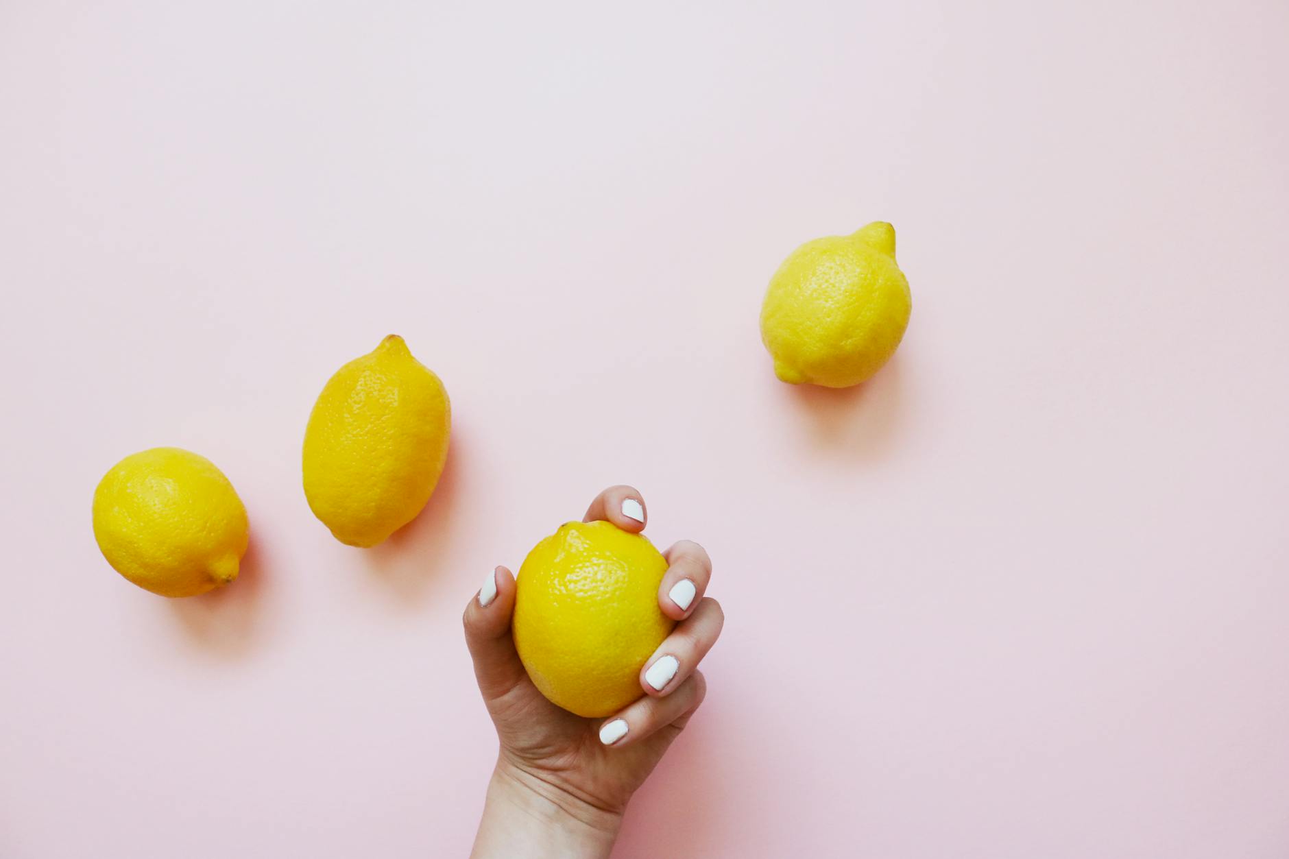 A hand holding a lemon on a soft pink background, representing the approach to difficult conversations about pleasure and intimacy.
