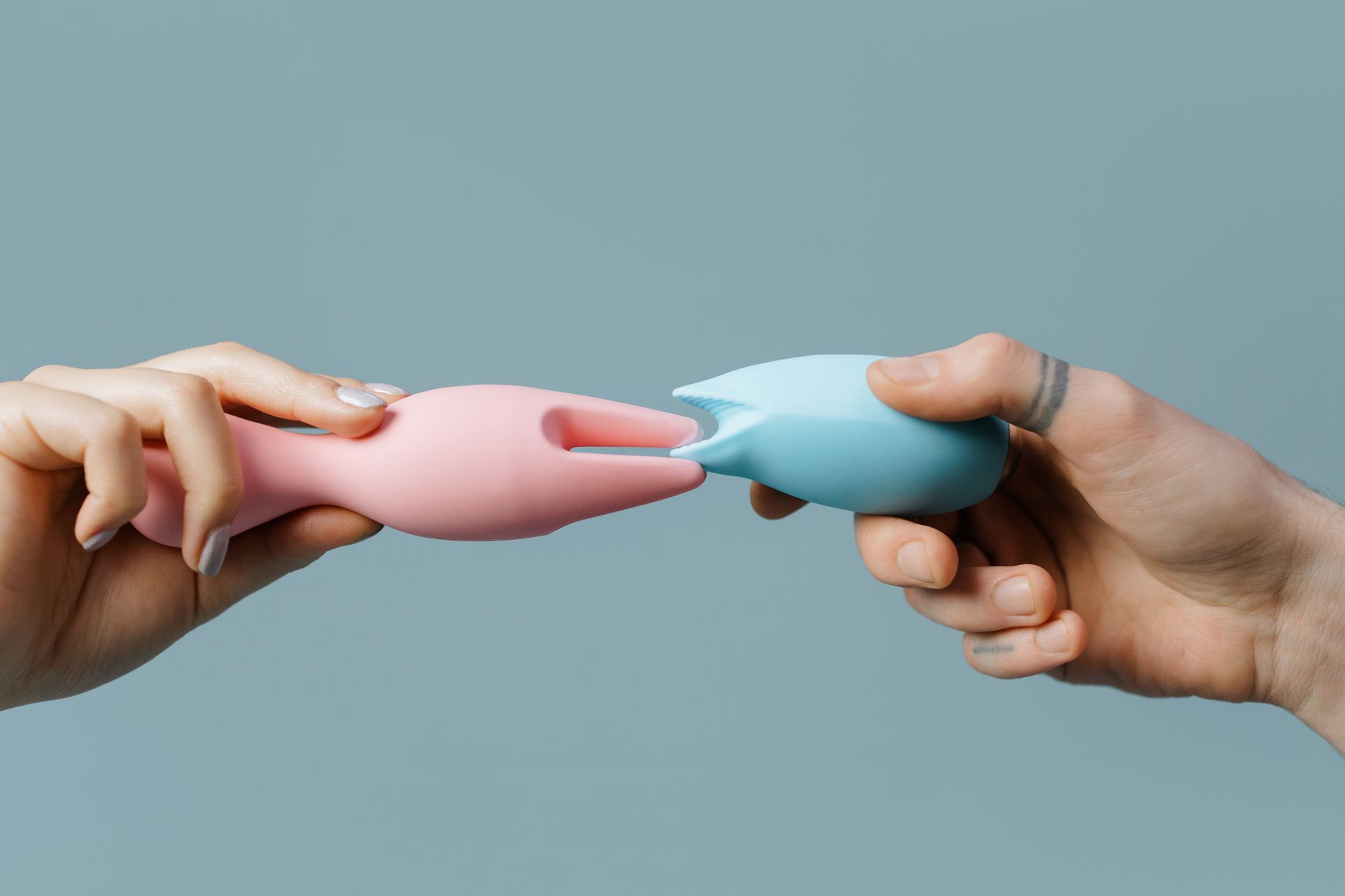 Hands holding pastel-colored silicone sex toys against a neutral background