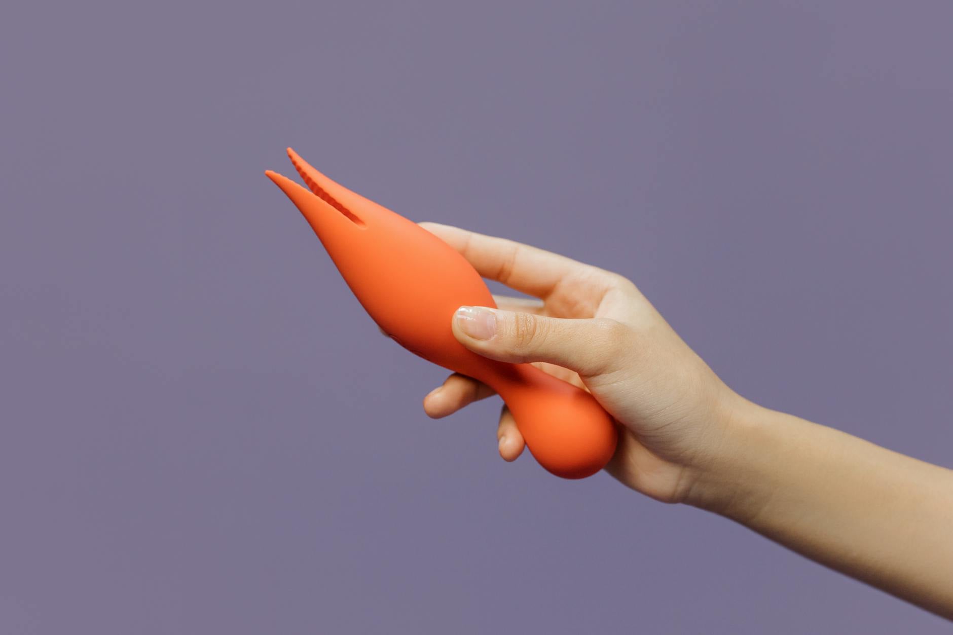 A hand holding a lemon-shaped clitoral vibrator against a minimalistic purple backdrop