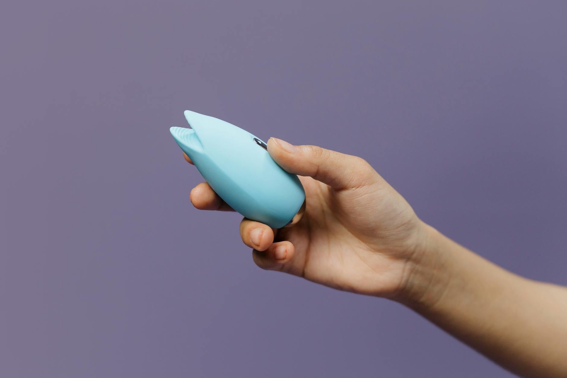 Hands holding a sleek blue lemon clitoral vibrator against a purple background