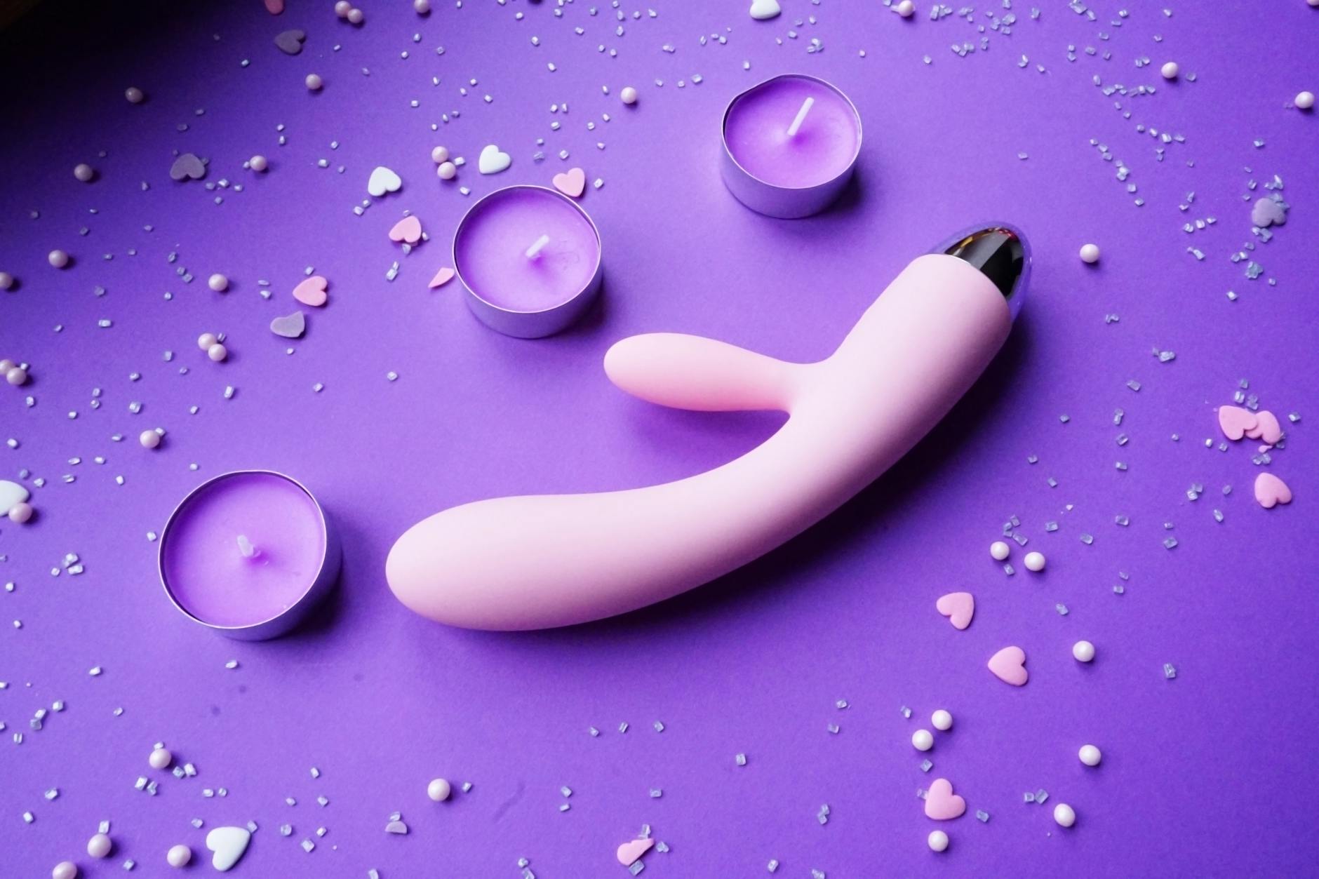Pink vibrator on purple background with heart confetti and candles, symbolizing maintaining pleasure in relationships.