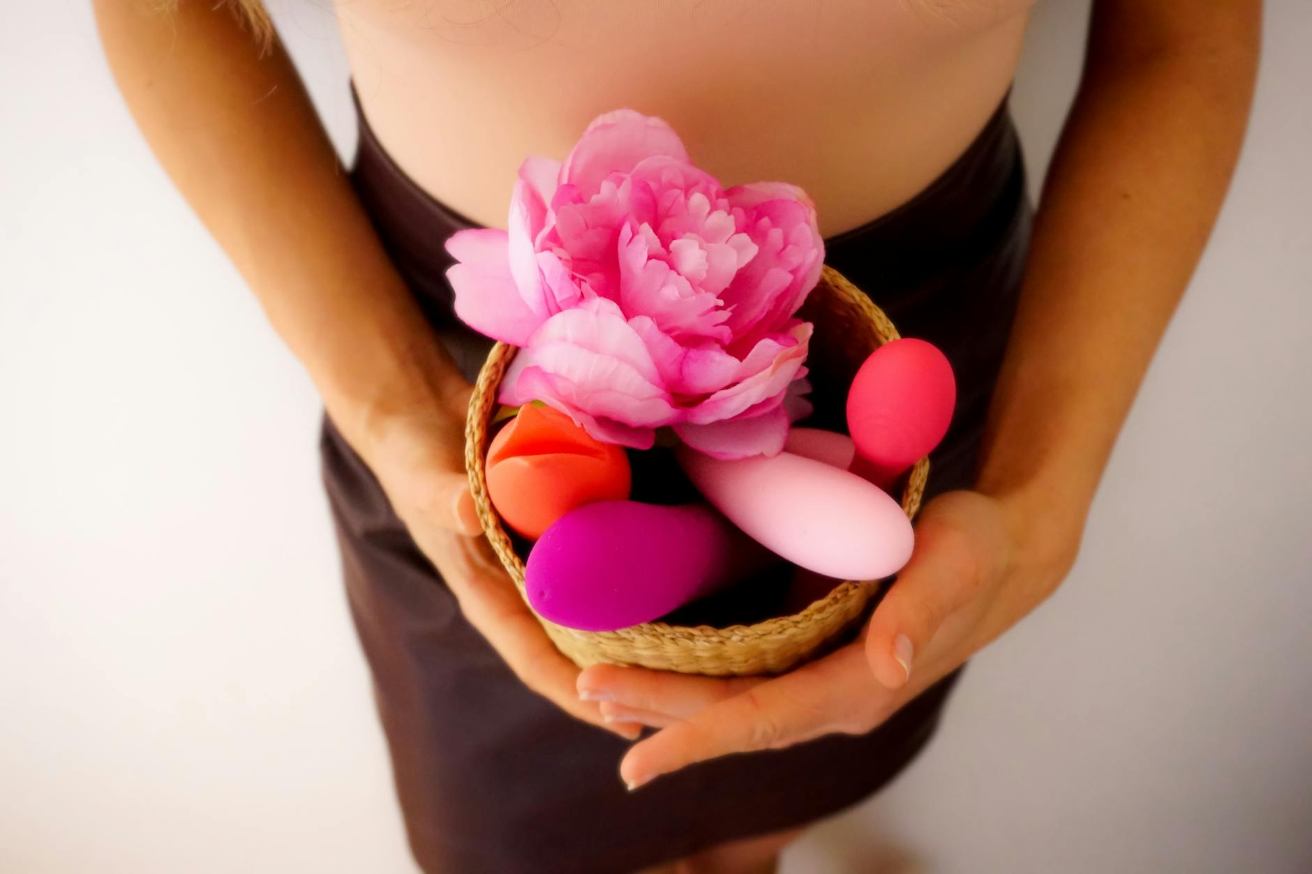 Woman with eyeglasses holding blue and pink silicone vibrators in a contemplative manner.